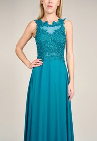 Türkisfarbenes Kleid mit floralem Spitzenoberteil, ärmellosem Design und fließendem Rock. Verfügt über zarte Perlenverzierungen und einen transparenten Dekolleté.