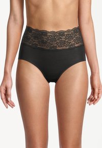 Mutande nere a vita alta con ampia vita in pizzo floreale indossate da una persona in piedi contro uno sfondo bianco semplice.