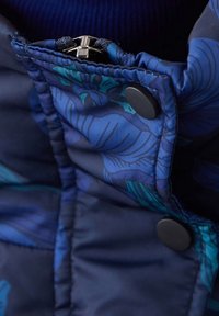 Giacca trapuntata blu navale con colletto a stampa floreale, dotata di zip, tessuto blu testurizzato e dettagli in plastica nera con bottoni a pressione.
