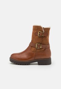 Braune Lederstiefelette mit doppelten Schnallenakzenten, strukturiertem Obermaterial und Kunstfellfutter. Verfügt über eine robuste Sohle mit einem leichten Absatz.