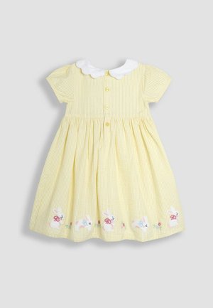 Keltainen raidallinen puuvillamekko, jossa on lyhyet hihat, valkoinen kaulus ja brodeerattuja pupuja helman kohdalla. Napitus edessä.