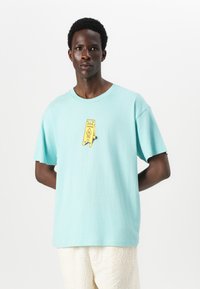 Light blue cotton t-shirt with a relaxed fit, featuring a yellow caution sign graphic on the chest and short sleeves.
