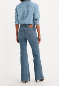 Blå denim flare jeans med hög midja, som har en läderetikett på baksidan och två bakfickor med sömnadsdetaljer.