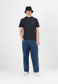 Navy blue cotton t-shirt with a crew neck and short sleeves, paired with light blue baggy denim jeans and white sneakers. Black bucket hat.