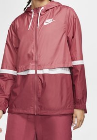 Veste à capuche Nike rose foncé, avec des accents blancs et une fermeture éclair. Comprend des poignets élastiques et une coupe courte. Matériau léger et résistant à l'eau.