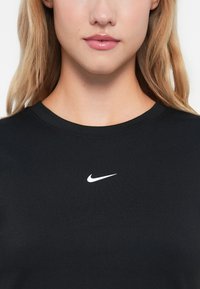 Černé tričko s kulatým výstřihem a krátkými rukávy. Na hrudi je uprostřed umístěno bílé logo Nike. Vyrobeno z hladké tkaniny.