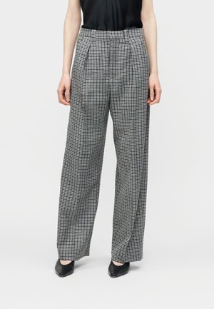 Kvinde iført sort-hvide ternede bukser med vide ben, sort ærmeløs top og sorte spidse sko.