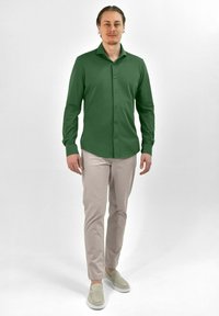 Groene langmatige shirt met knoopsluiting, met een semi-aangesneden ontwerp. Gecombineerd met lichtbeige broeken en grijze instap schoenen.