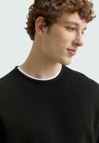 Schwarzer gerippter Pullover mit rundem Ausschnitt und kontrastierendem weißen Innenkragen. Glatte Textur und taillierte Passform.