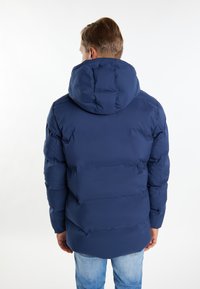 Navy blå pufferjakke med hætte, der har et quiltet design, elastiske manchetter og en let forlænget bagkant.
