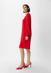 Rotes, langärmliges Shiftkleid mit lockerer Passform, glatter Textur und geknöpften Manschetten. Kombiniert mit roten Slingback-High Heels mit spitzer Zehenform.
