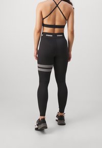Leggings neri a vita alta con un accento a strisce testurizzate sul lato. Presentano una vestibilità aderente con un design riflettente e un tessuto morbido.