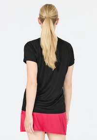 Svart träningsskjorta med korta ärmar, i kombination med en rosa kjol. Slät textur, figursydd design, inga synliga logotyper eller dekorationer.