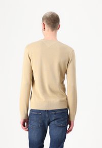 Beige strikkegenser med lange ermer, ribbede mansjetter og kant, samt V-formet bakhals, kombinert med mørkeblå jeans.