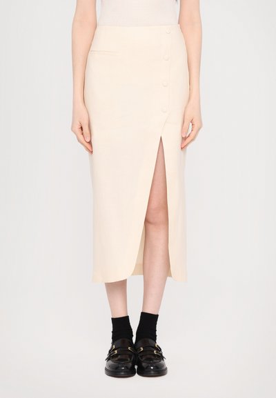 Beige midi skirt with a front slit and button detailing, featuring a smooth fabric and side pockets. Paired with black socks and loafers.