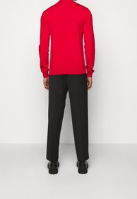 Czerwony sweter z długim rękawem i wysokim kołnierzem, połączony z czarnymi, dopasowanymi spodniami. Strój ma luźny krój i gładką fakturę.