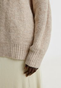 Hellbeige, gerippter Pullover aus weichem, flauschigem Material, mit langen Ärmeln in lockerer Passform und hohem gerippten Bündchen.