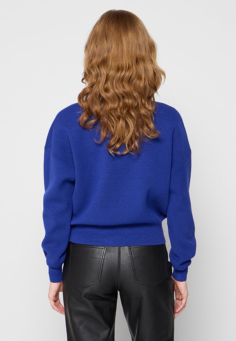 Królewsko niebieski sweter dzianinowy o luźnym kroju, z prążkowanymi mankietami i dołem oraz obniżonymi szwami na ramionach, w zestawieniu z czarnymi spodniami z sztucznej skóry.