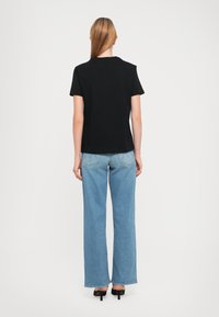 Schwarzes Baumwoll-T-Shirt mit kurzen Ärmeln und lässiger Passform, kombiniert mit hellblauen weit geschnittenen Jeans und schwarzen High Heels.