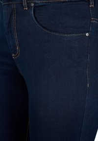 Jeans de mezclilla azul oscuro con una textura suave, costuras visibles en un contraste naranja y un diseño estándar de bolsillo frontal.