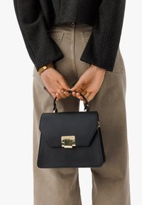 Svart läderhandväska med en strukturerad design, guldfärgade detaljer och ett handtag på toppen. Har en klaffstängning med en metallisk accent.