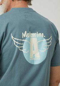 Camiseta azul de algodón con un gran gráfico blanco que incluye "MotorsInc." arriba de un diseño circular y alas estilizadas que rodean la letra "A".