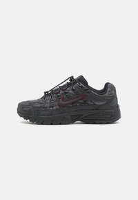 Sapatos atléticos pretos com um cabedal texturizado, sistema de atacadores integrado e um detalhe da swoosh da Nike em bordô. Sola de borracha grossa para tração.