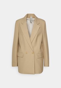 Blazer beige de doble botonadura hecho de tejido suave, con solapas de pico, dos bolsillos frontales y acentos de botones dorados.