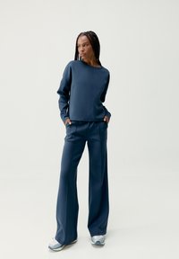 Námornícky modrá mikina a široké nohavice vyrobené z hladkej, elastickej látky. Obsahuje jednoduchý dizajn s minimálnymi švami a prednými vreckami.