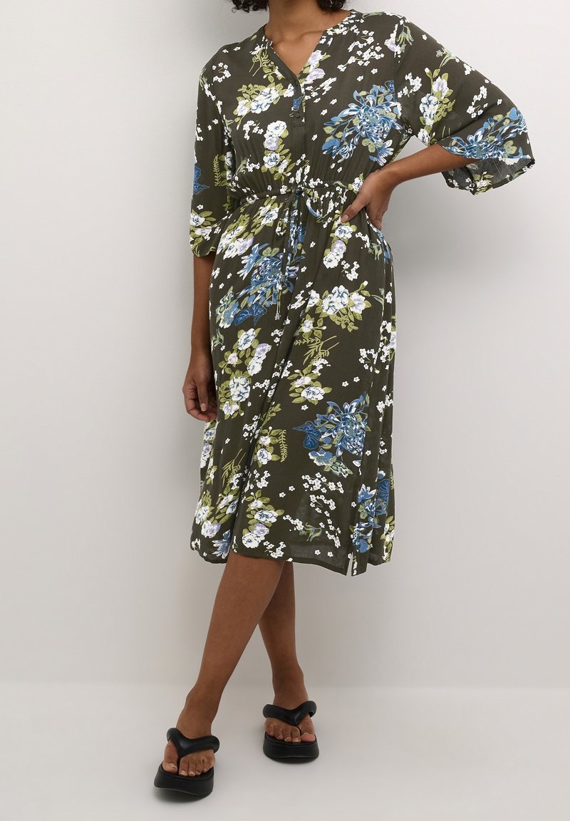 Florales Midikleid in Olivgrün. Mit blauen und weißen Blumen, tailliert, V-Ausschnitt und lockeren Ärmeln. Hergestellt aus leichtem Stoff.