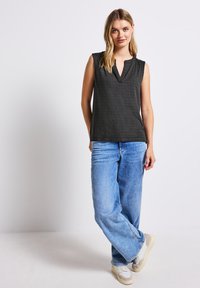 Svart ärmlös topp med en strukturerad geometrisk mönstring, V-ringning, matchad med ljusblå vida jeans och vita sneakers.