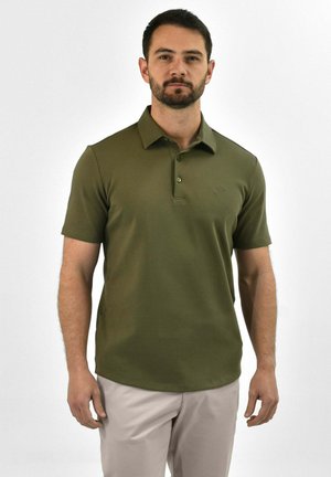 Olijfgroene polo met korte mouwen, drie-knops knoopsluiting en een subtiele logo op de borst; gladde textuur. Slanke pasvorm.