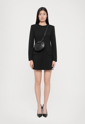 Robe noire à manches longues, avec poches avant, accompagnée d'un petit sac crossbody noir de forme courbe et avec des accents en chaîne.