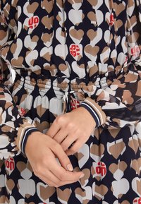 Bunt gestreiftes Kleid mit Herzmuster in Beige, Weiß und Rot auf einem dunkelblauen Hintergrund. Verfügt über einen elastischen Bund und Ärmelbündchen mit Streifen.