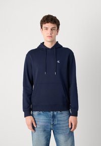 Felpa con cappuccio blu navy in misto cotone, dotata di tasca a marsupio, polsini a costine e lacci pendenti. Piccolo logo sul petto.