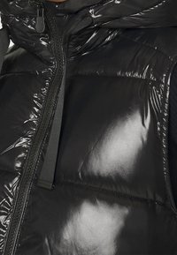 Czarna pikowana kamizelka o błyszczącym wykończeniu, z frontowym zamkiem błyskawicznym i teksturowanymi detalami, zaprojektowana z kapturem i kontrastowym materiałem po bokach.