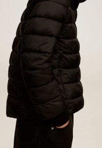 Zwarte pufferjas met doorgestikte delen, een hoge kraag en een verstelbare trekkoord. Gladde, glanzende stof met een ontspannen pasvorm.