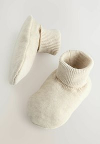 Chaussons ronds et doux en matière tricotée crème. Design à revers avec une texture côtelée et une semelle lisse. Style minimaliste sans marquage visible.
