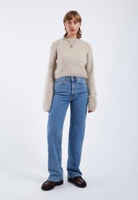 Ljusbeige fluffig tröja med långa, lösa ärmar, kombinerad med högmidjade blå raka jeans och svarta platåskor.