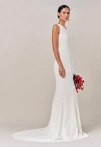 Vestido de novia blanco sin mangas con una silueta ajustada y cola, con botones a lo largo de la espalda y una textura lisa similar al satén.