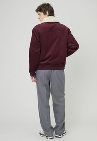 Veste en velours côtelé bordeaux avec col en fausse fourrure beige, ourlet et poignets côtelés, associée à un pantalon tailleur gris clair et des baskets blanches.