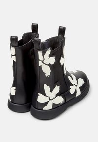 Bottines noires avec un grand imprimé floral blanc, des panneaux élastiques sur les côtés et des languettes à l'arrière et à l'avant.