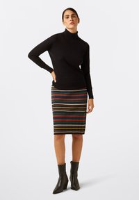 Zwarte geribbelde coltrui gecombineerd met een knie-lange gestreepte rok in groen, rood en geel. Zwarte enkelboots maken de look af.