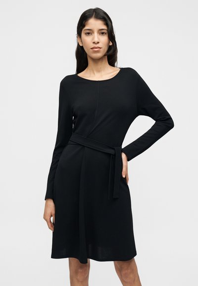 Μαύρο φόρεμα με μακριά μανίκια, στρογγυλή λαιμόκοψη, ζώνη στη μέση και ομαλή υφή, με ένα ντραπέ σχέδιο που φτάνει μέχρι τα γόνατα.