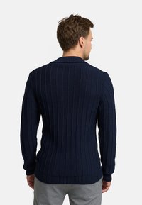 Dunkelblauer gerippter Cardigan mit langen Ärmeln und Schalkragen, ausgestattet mit einem strukturierten Strickmuster und einem taillierten Saum.