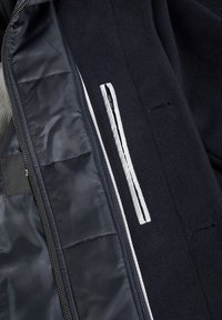 El interior de la chaqueta navy incluye un forro suave, un bolsillo con cremallera y una tela texturizada. Los acentos incluyen un detalle a rayas a lo largo del bolsillo.