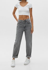 Jeans grises de cintura alta con un corte relajado, con dobladillos enrollados. Combinados con una camiseta blanca de cuello en V corta y zapatillas blancas.