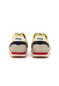 Par de zapatillas en amarillo, negro y beige con suelas en rojo y beige, mostrando la parte trasera con la marca 'mtng.' y '1967' en cada talón.