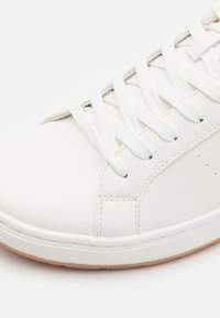 Hvit lær sneaker med teksturert overdel, flate lisser og gummisåle. Har et subtilt stikkmønster og minimale perforeringer for pusteevne.