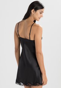 Camiseta de satén negra con tirantes delgados ajustables y un borde de encaje a lo largo del dobladillo. La tela tiene una textura suave y brillante.